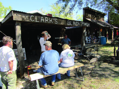 people sitting outside of a building with a sign reading "Clark's Blacksmith."